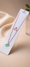 A delicate rose gold chain necklace with a round light green pendant, displayed on a white card labeled 'Beetly' alongside matching rose gold stud earrings, set against a warm beige background.